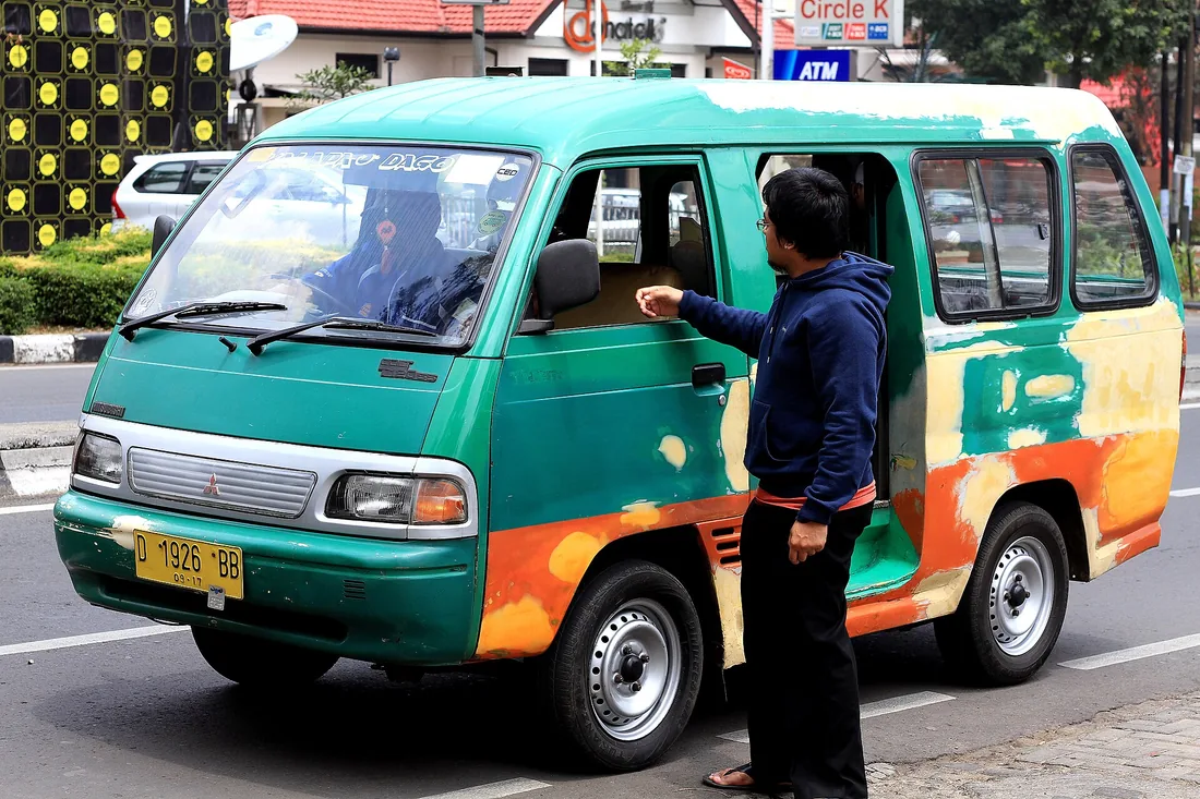 Angkot jurusan Kalapa-Dago berwarna hijau oranye berhenti di tepi Jalan Dago, seorang penumpang berbicara dengan sopir