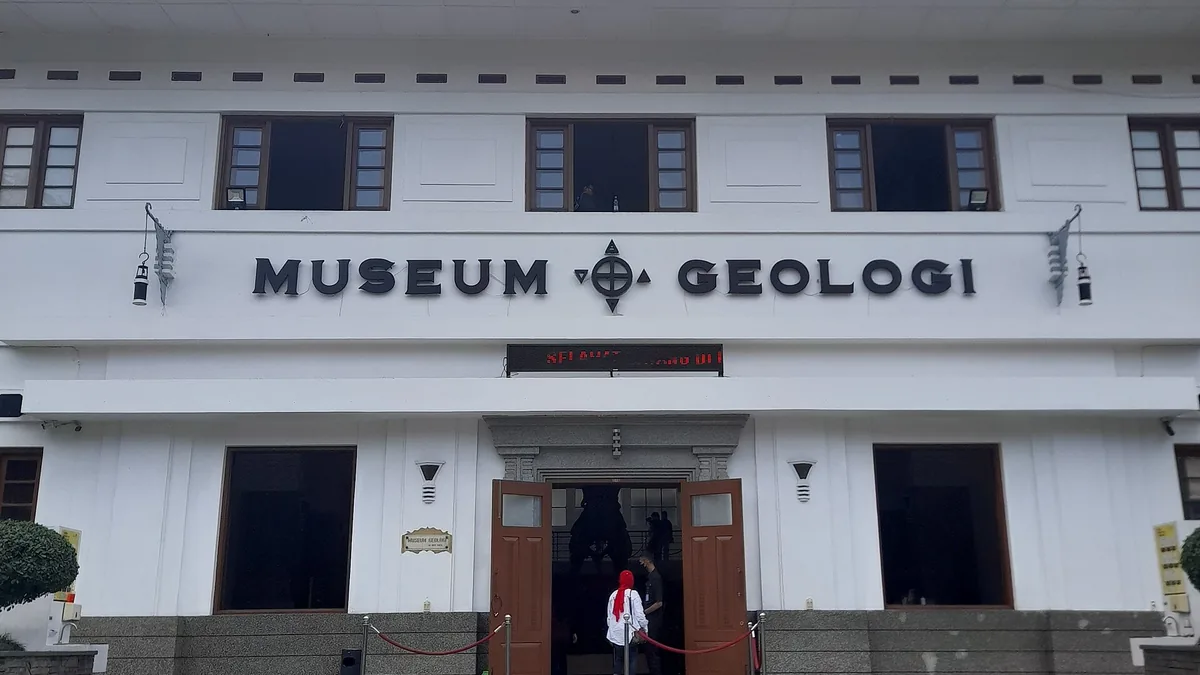 Fasad depan Museum Geologi Bandung berwarna putih dengan huruf timbul MUSEUM GEOLOGI dan pengunjung di pintu masuk