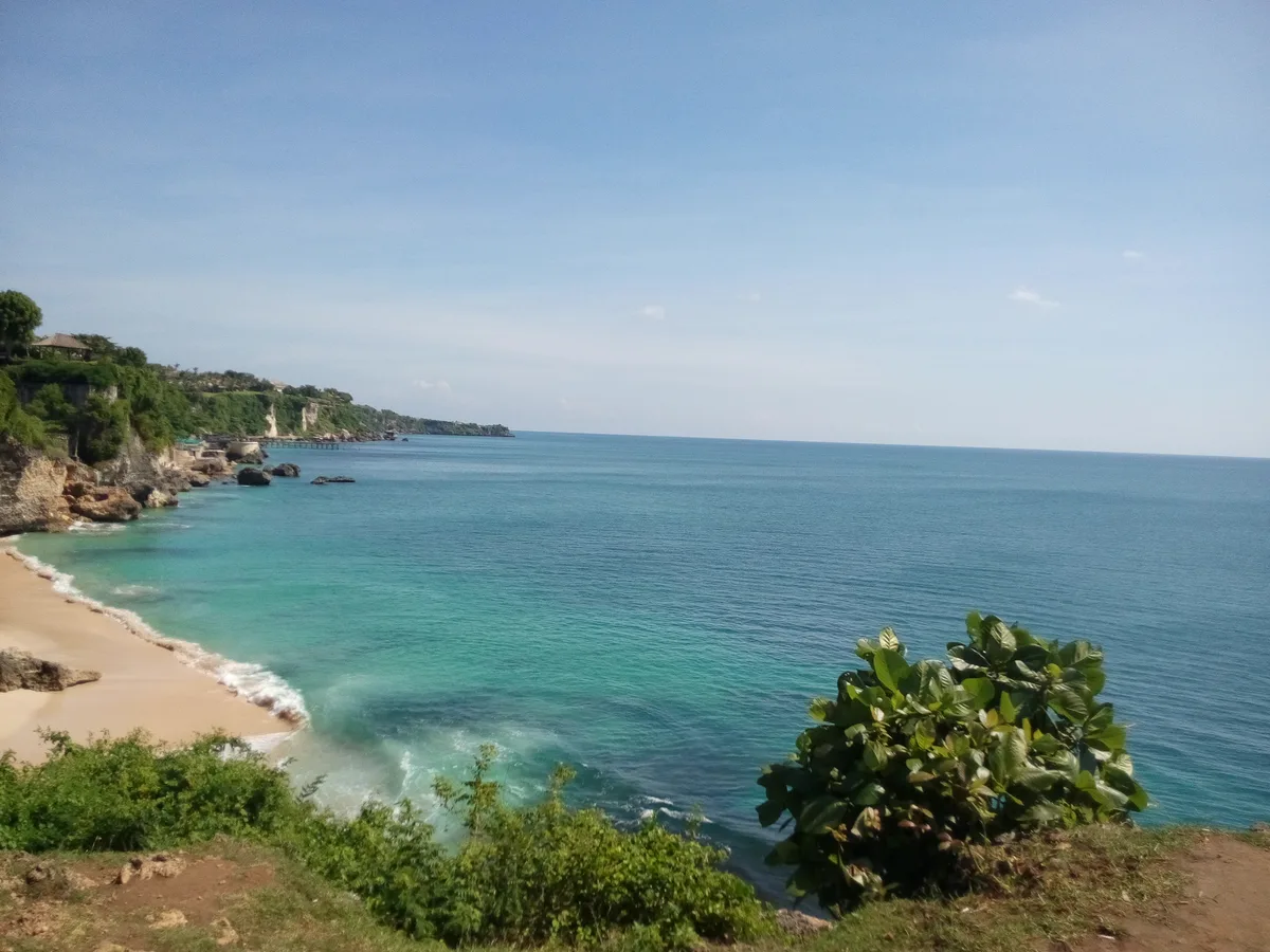 Teluk Pantai Padang Padang dilihat dari jalur tebing di atasnya, air toska dan garis pasir putih di bawah