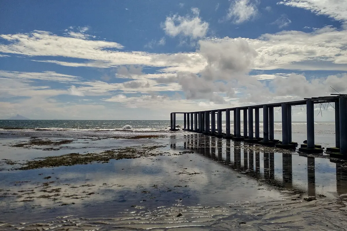 Hamparan karang tersingkap saat air surut di Pantai Anyer dengan struktur dermaga beton memanjang ke laut
