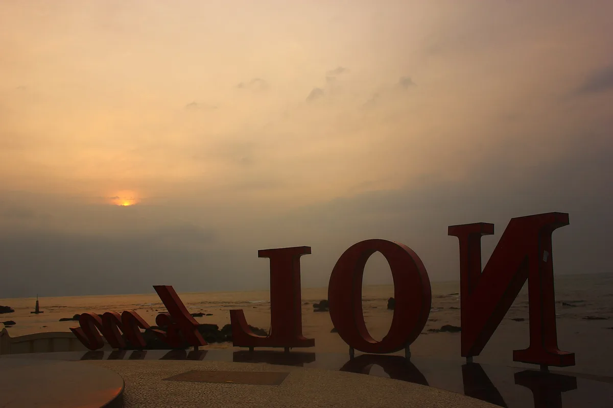 Tugu huruf Nol Km Anyer-Panarukan di tepi Pantai Anyer difoto dari sisi belakang dengan matahari rendah di belakangnya