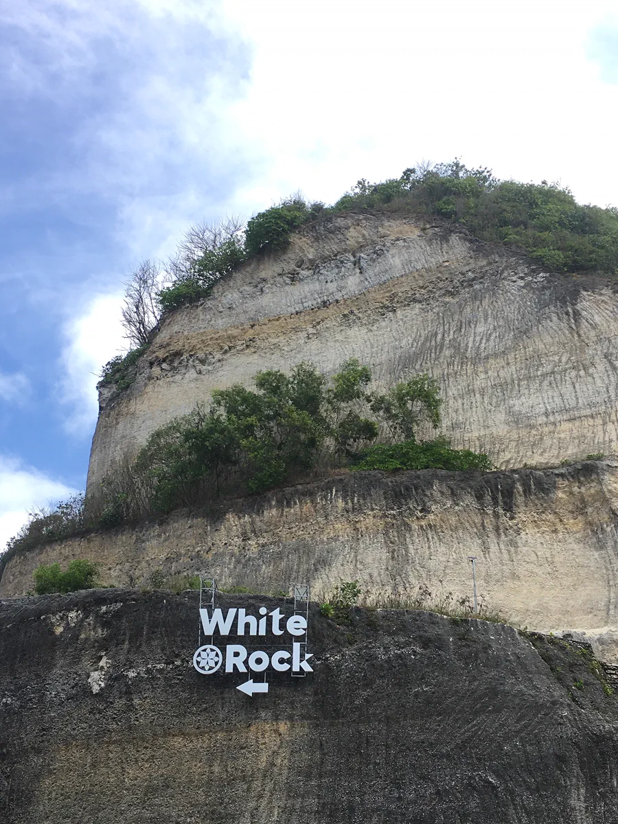 Papan penunjuk arah bertuliskan White Rock menempel di dinding karang di bawah tebing kapur Pantai Melasti