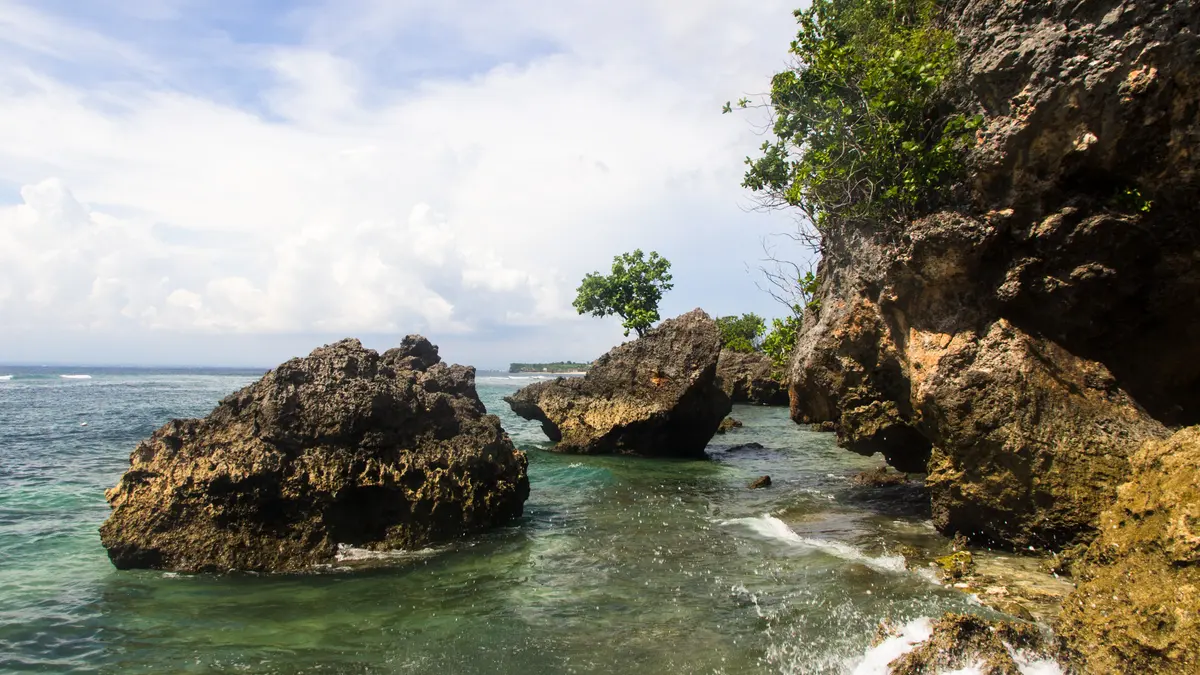 Batu karang besar berdiri di air toska di sisi Pantai Padang Padang, Pecatu, Bali