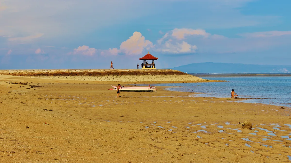 Air dangkal dan tenang di Pantai Sanur dengan bale beratap merah di ujung daratan berpasir