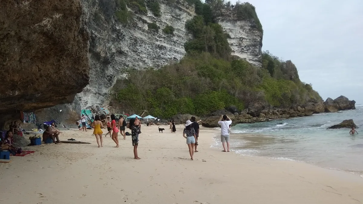 Pengunjung berjalan di pasir Pantai Suluban dengan dinding tebing karang menjulang di belakangnya