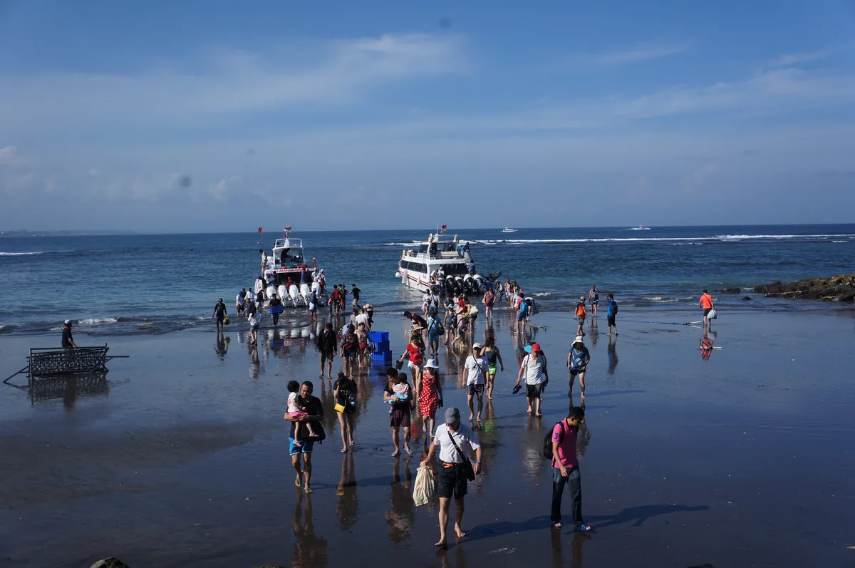 Rombongan wisatawan berjalan di hamparan pasir basah setelah turun dari dua fast boat di Pantai Sanur