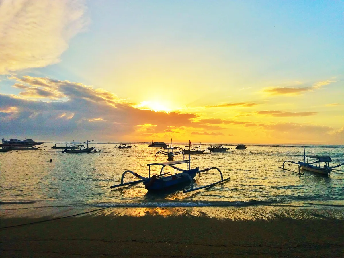 Matahari terbit keemasan di Pantai Sanur dengan beberapa jukung nelayan mengapung di air tenang