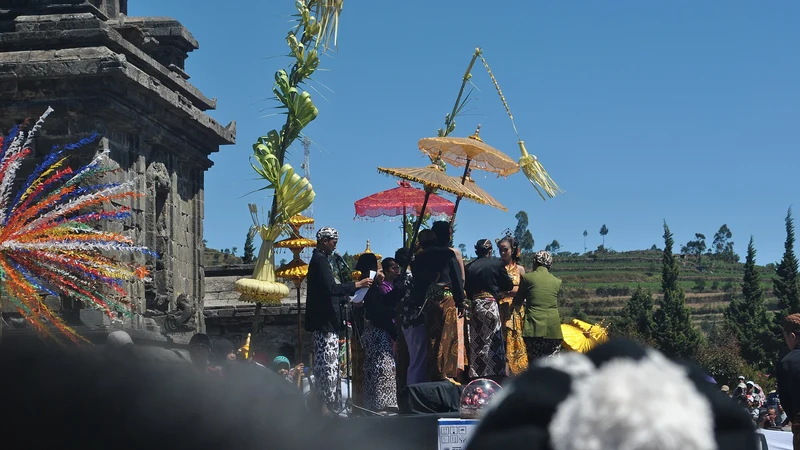 Prosesi ruwatan pemotongan rambut gimbal anak Dieng dengan payung hias dan gunungan di depan candi