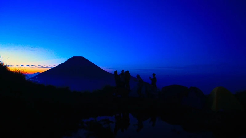 Wisatawan menunggu matahari terbit di puncak Bukit Sikunir dengan siluet Gunung Sindoro di kejauhan